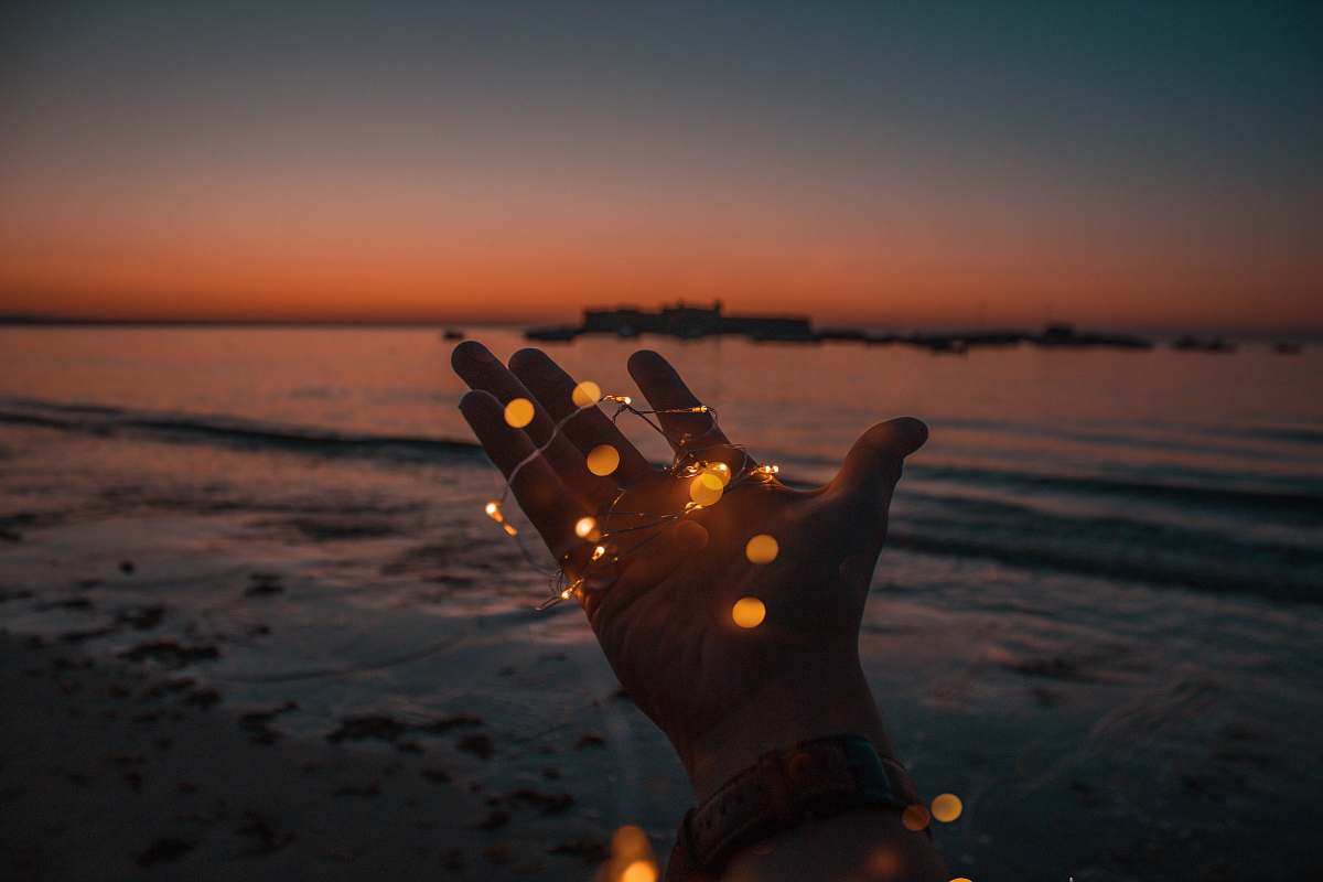 fairy lights person with string lights on left hand beach